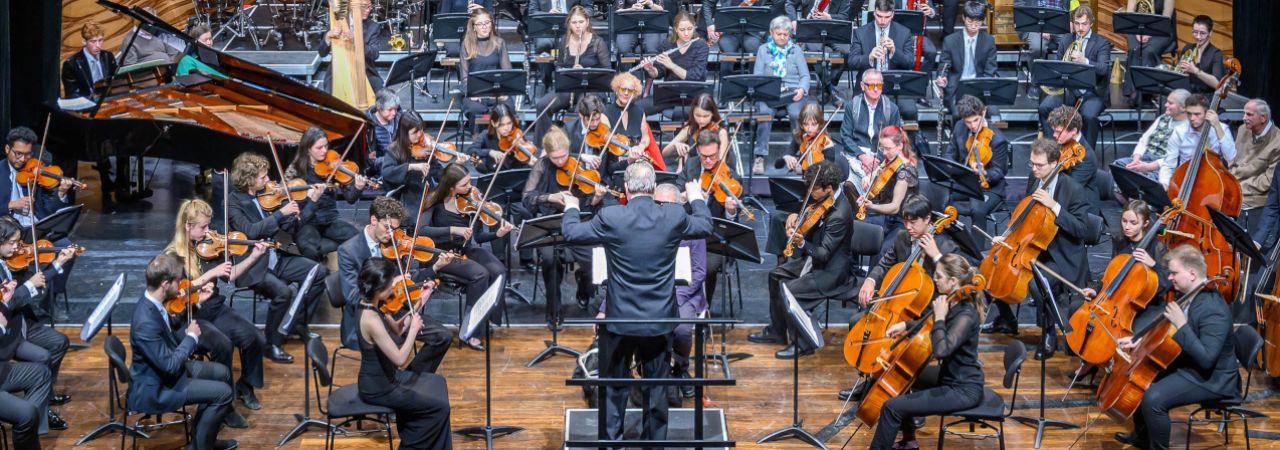 Mitglieder des Blinden- und Sehbehindertenverbandes Österreich bei einem Konzert des MUK.sinfonieorchester zwischen den Musiker*innen auf der Bühne